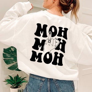 Pode incluir: Camisola branca com texto preto que diz "MOH MOH MOH" com uma ilustra&ccedil;&atilde;o em preto e branco de uma m&atilde;o a fazer o dedo do meio no meio do texto.