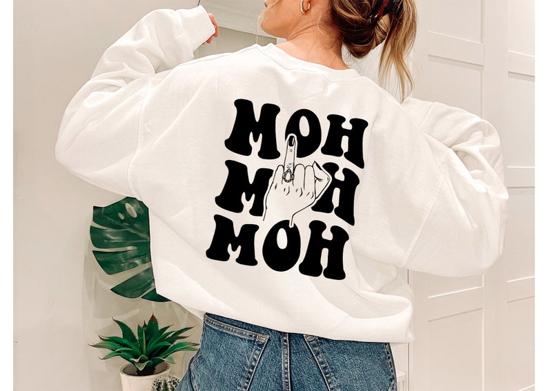 Pode incluir: Camisola branca com texto preto que diz "MOH MOH MOH" com uma ilustra&ccedil;&atilde;o em preto e branco de uma m&atilde;o a fazer o dedo do meio no meio do texto.
