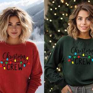 May include: Two women wearing long-sleeved sweatshirts with the text "Christmas Crew" and a string of colorful lights. The sweatshirt on the left is red and the sweatshirt on the right is green.