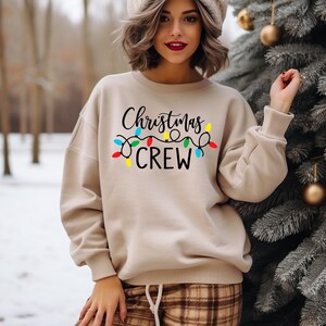 May include: A beige sweatshirt with the text "Christmas Crew" and a string of colorful Christmas lights printed on the front.
