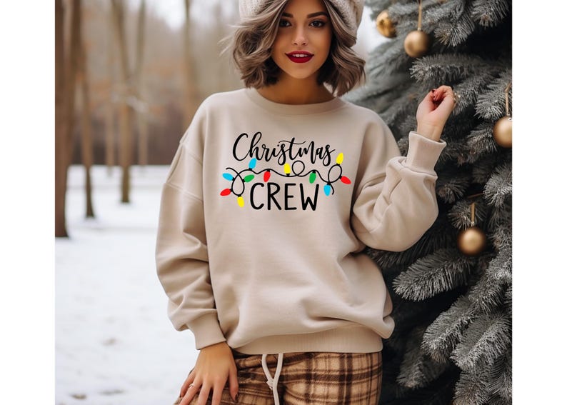 May include: A beige sweatshirt with the text "Christmas Crew" and a string of colorful Christmas lights printed on the front.