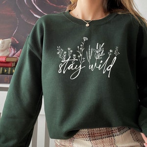 May include: A dark green sweatshirt with a white floral design and the text "stay wild" printed on the front.
