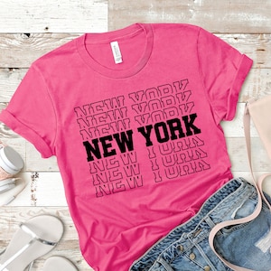 May include: A pink t-shirt with the text "NEW YORK" repeated in a stacked pattern in black.