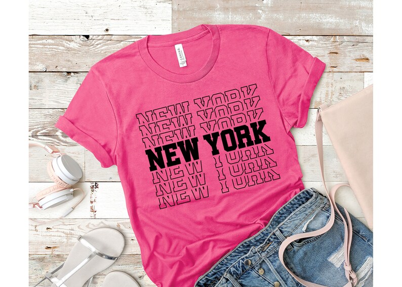 May include: A pink t-shirt with the text "NEW YORK" repeated in a stacked pattern in black.