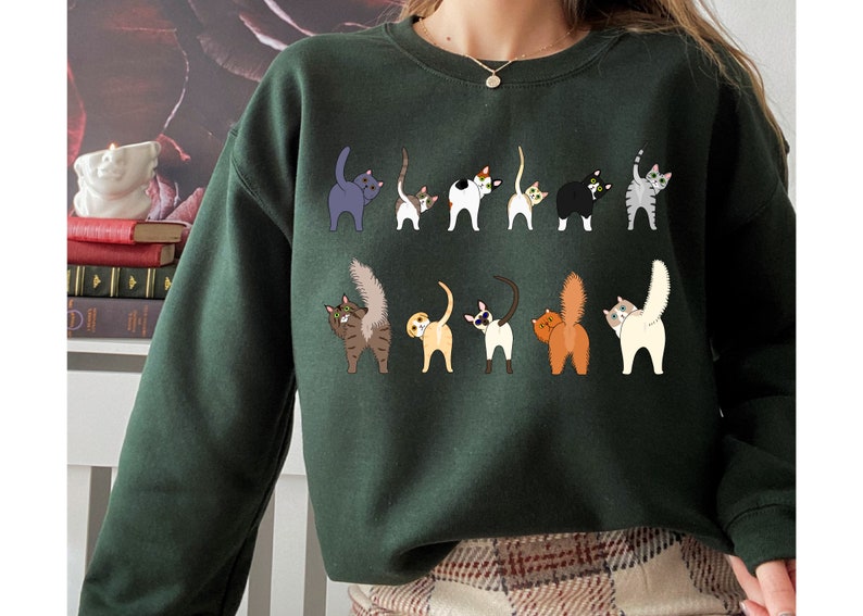 May include: A dark green sweatshirt with a print of multiple cats with their tails up in the air. The cats are in various colors and patterns.