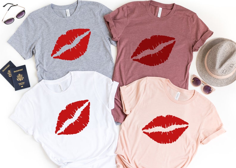 May include: Four t-shirts with a red lip print design. The shirts are in different colors: gray, maroon, white, and pink.