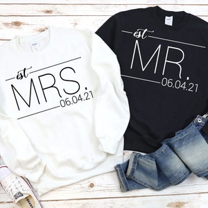 May include: Two white sweatshirts with black text. One says "est. MRS. -06.04.21" and the other says "est. MR. -06.04.21".