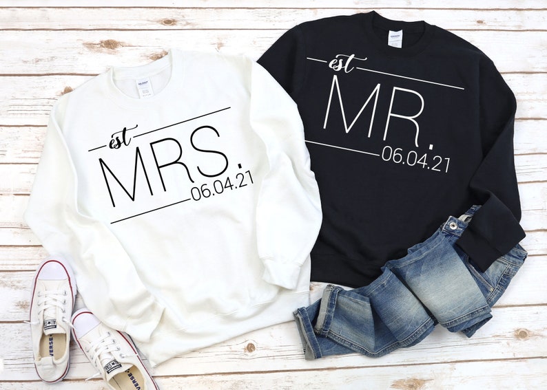 May include: Two white sweatshirts with black text. One says "est. MRS. -06.04.21" and the other says "est. MR. -06.04.21".