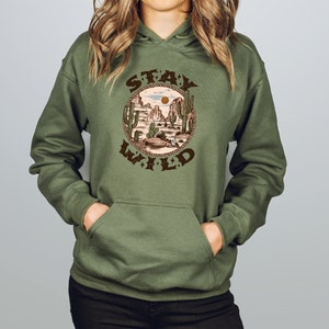 May include: A green hooded sweatshirt with a brown graphic print of a desert landscape with cacti and the text "STAY WILD" in a circle.