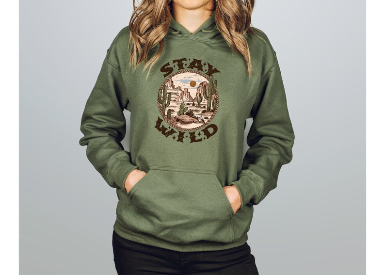 May include: A green hooded sweatshirt with a brown graphic print of a desert landscape with cacti and the text "STAY WILD" in a circle.