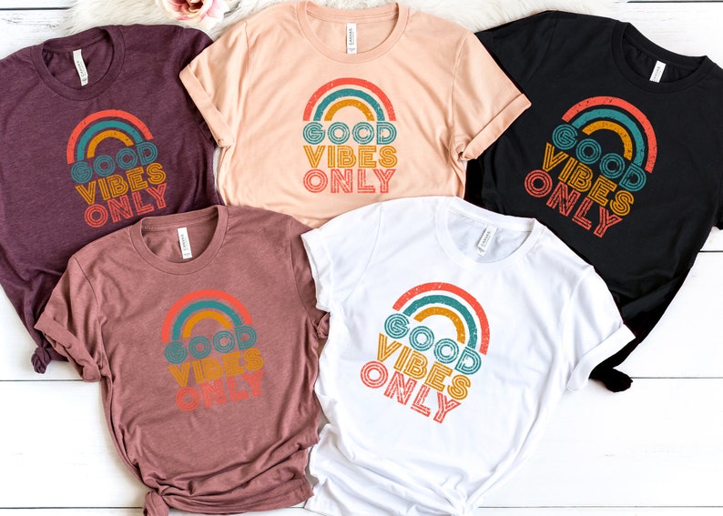 May include: Five t-shirts in different colors with the text "Good Vibes Only" printed on them in a retro rainbow design.