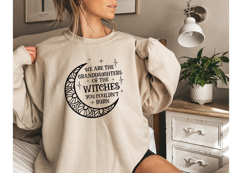May include: A beige sweatshirt with a black crescent moon graphic and the text "We are the granddaughters of the witches you couldn't burn".