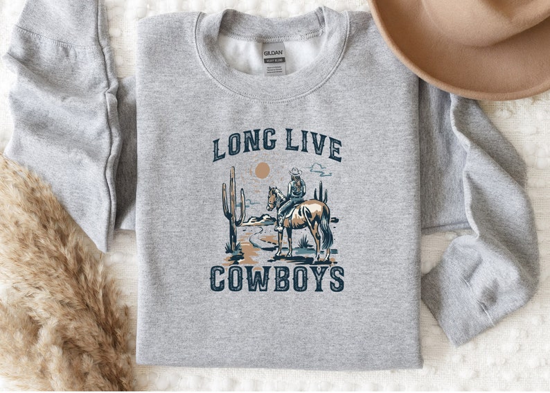 May include: A gray sweatshirt with a graphic print of a cowboy riding a horse in a desert landscape. The text "Long Live Cowboys" is printed on the sweatshirt.