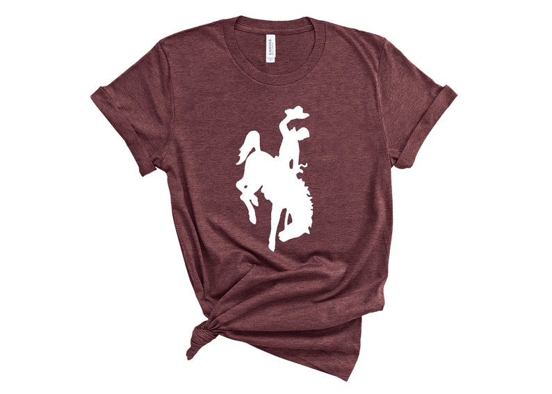 May include: A maroon t-shirt with a white silhouette of a cowboy riding a bucking horse.