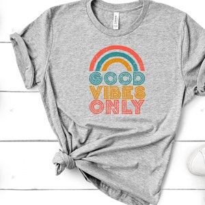 May include: A gray t-shirt with a rainbow graphic and the text "GOOD VIBES ONLY" in a retro font.