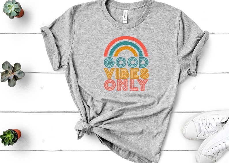 May include: A gray t-shirt with a rainbow graphic and the text "GOOD VIBES ONLY" in a retro font.