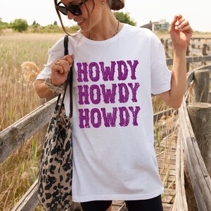 Op de afbeelding: Wit T-shirt met de tekst "Howdy Howdy Howdy" in paars.