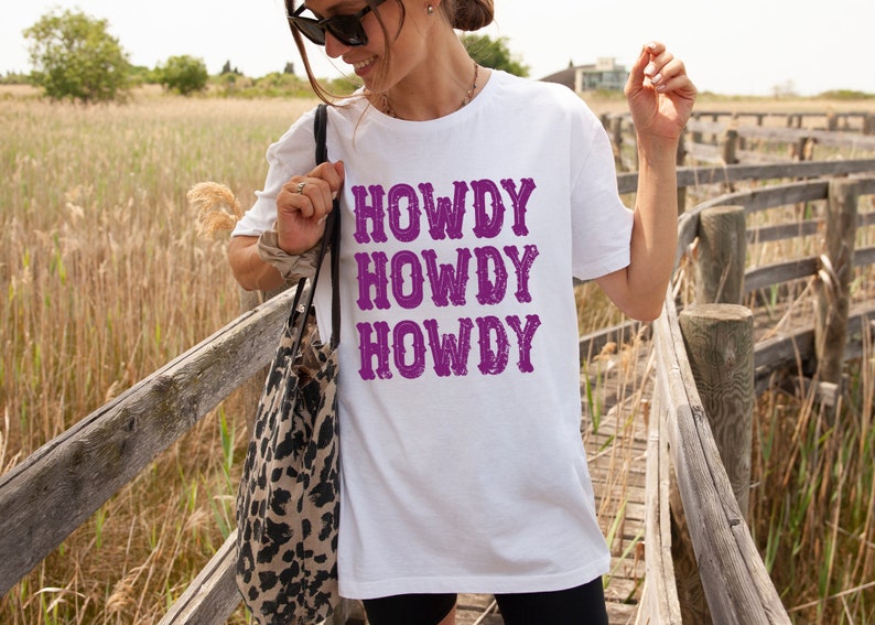 Op de afbeelding: Wit T-shirt met de tekst "Howdy Howdy Howdy" in paars.