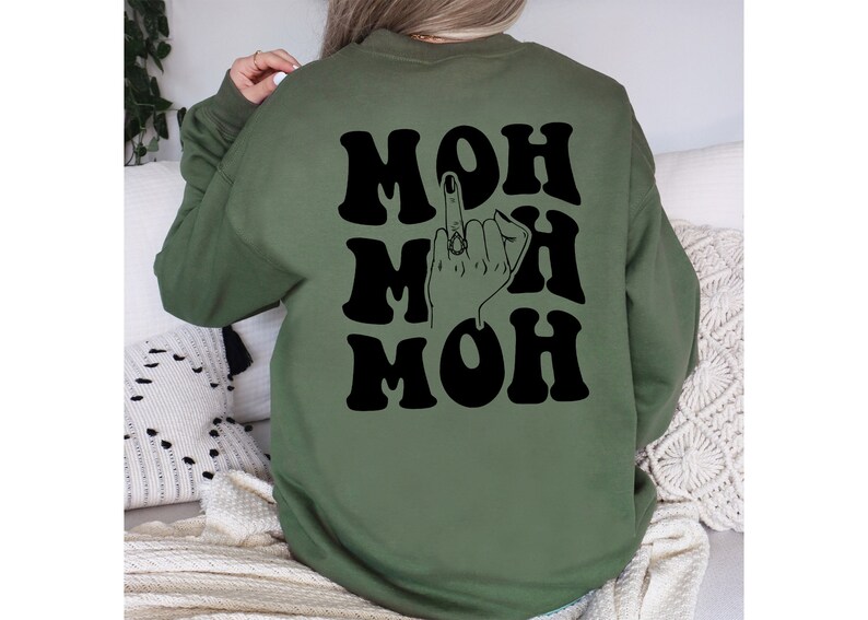 Pode incluir: Camisola verde com texto preto que diz "MOH MOH MOH" e uma ilustra&ccedil;&atilde;o preta de uma m&atilde;o a fazer o dedo do meio com um anel no dedo do meio.