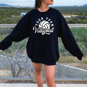Puede incluir: Sudadera negra con texto blanco que dice "Your Team Volleyball" y un gr&aacute;fico de voleibol blanco.
