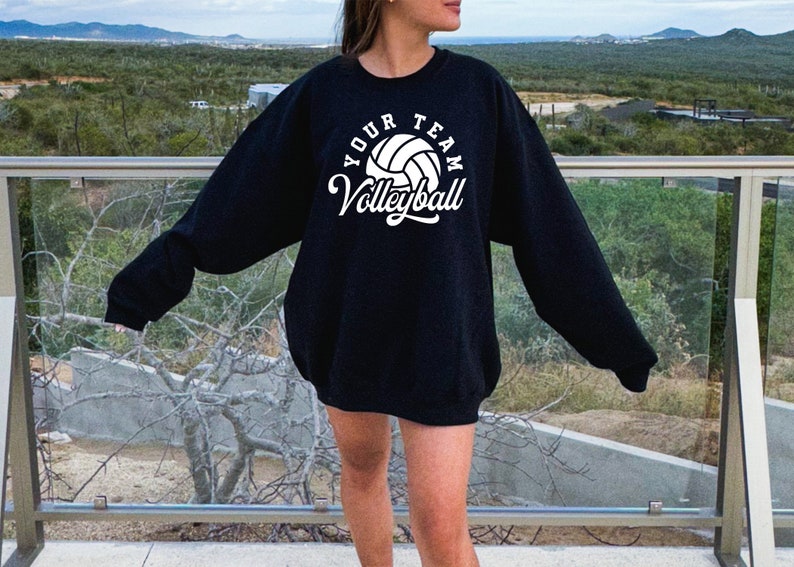 Puede incluir: Sudadera negra con texto blanco que dice "Your Team Volleyball" y un gr&aacute;fico de voleibol blanco.