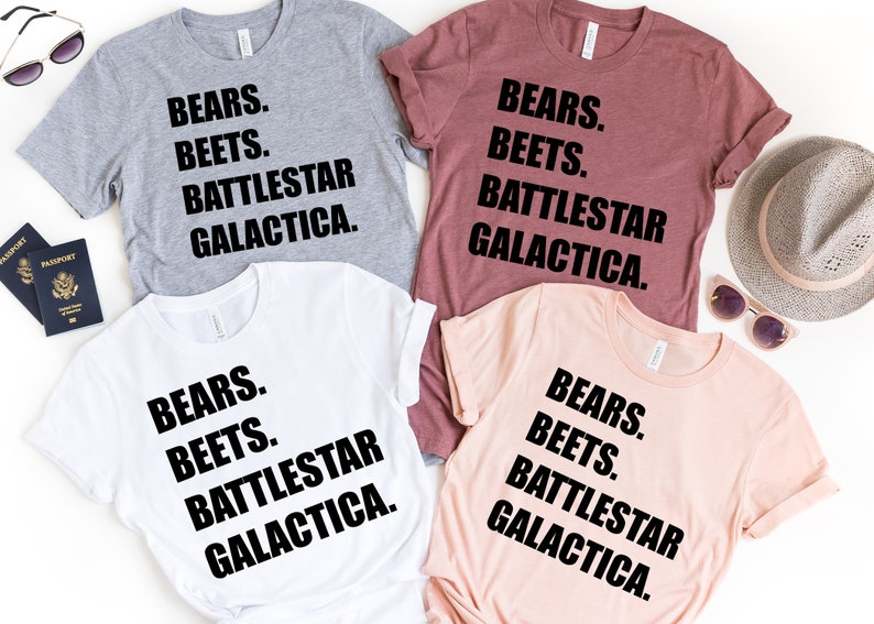 May include: Four t-shirts in gray, maroon, white, and peach, each with the text "BEARS. BEETS. BATTLESTAR GALACTICA." in black. Sunglasses and passports are visible in the background.