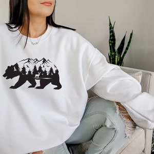 May include: White sweatshirt with a black silhouette of a bear with mountains and trees inside the bear's body.