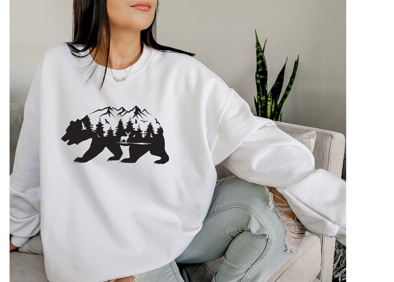 May include: White sweatshirt with a black silhouette of a bear with mountains and trees inside the bear's body.