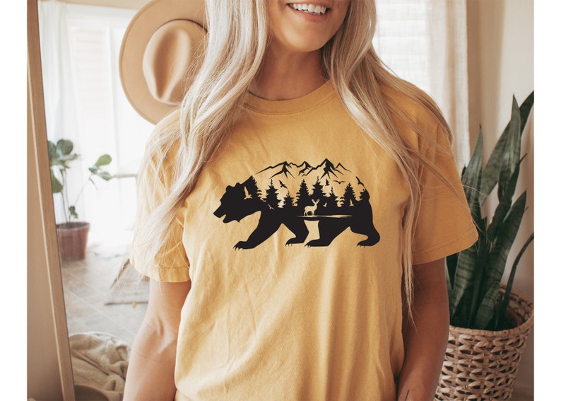 May include: A yellow t-shirt with a black silhouette of a bear with mountains, trees, and a deer inside the bear's outline.