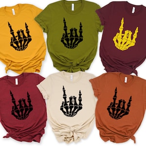 Puede incluir: Seis camisetas de manga corta en varios colores, como amarillo mostaza, verde oliva y burdeos. Cada camiseta presenta un gr&aacute;fico de mano de esqueleto negro en un gesto de rock and roll. Las camisetas est&aacute;n hechas de un material suave.
