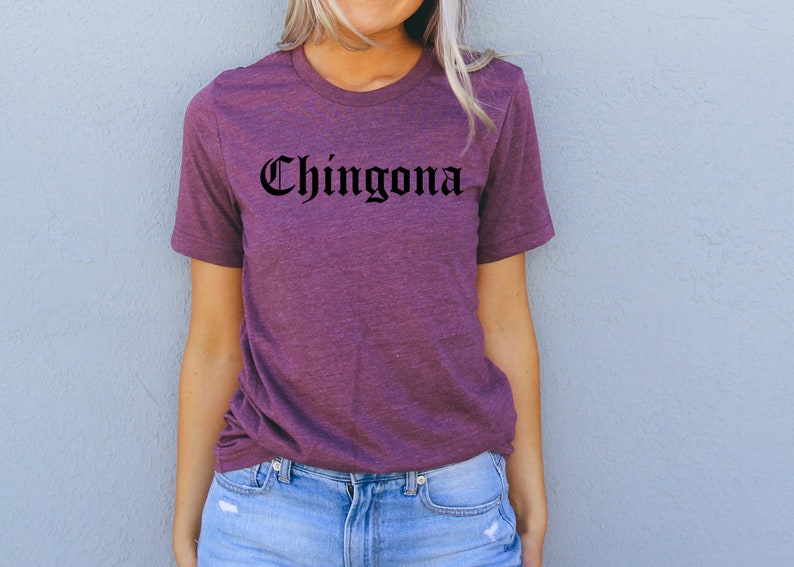 May include: A purple t-shirt with the word "Chingona" printed in black gothic lettering.