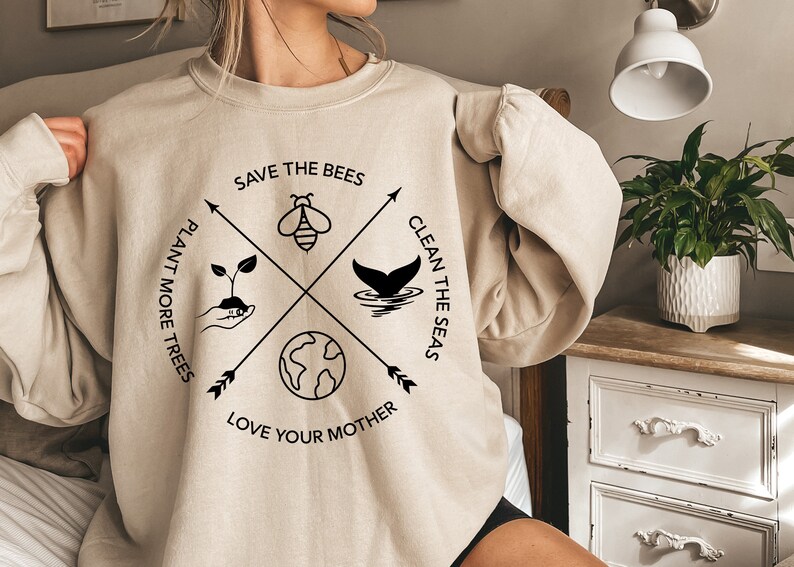 Może przedstawiać: Beżowa bluza z czarnym nadrukiem graficznym przedstawiającym pszczołę, ogon wieloryba, kiełek i glob. Tekst głosi "Save the Bees", "Plant More Trees", "Clean the Seas" i "Love Your Mother".