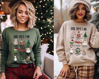 May include: Two women wearing green and beige sweatshirts with a Christmas-themed design that says "God Says I Am..." with a list of positive attributes. The design features a Christmas tree, a Grinch, a snowman, a peace sign, and a reindeer.