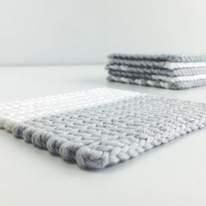 May include: A set of four gray and white woven coasters. The coasters are made of a thick, textured yarn and have a subtle ombre effect.