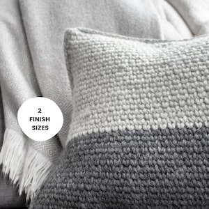 Könnte beinhalten: Ein zweifarbiges graues Zierkissen mit einem strukturierten Strickdesign. Das Kissen ist rechteckig und hat eine hellgraue obere Hälfte und eine dunkelgraue untere Hälfte. Eine hellgraue Decke ist im Hintergrund. Der Text "2 Finish Sizes" ist enthalten.