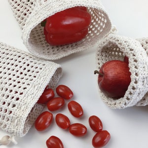 Puede incluir: Tres bolsas de malla de crochet blancas para productos con productos rojos. Una bolsa contiene un pimiento rojo, otra una manzana roja y la tercera bolsa tiene tomates cherry rojos que se derraman.