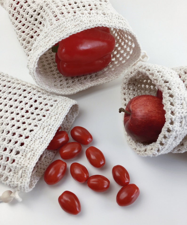 Puede incluir: Tres bolsas de malla de crochet blancas para productos con productos rojos. Una bolsa contiene un pimiento rojo, otra una manzana roja y la tercera bolsa tiene tomates cherry rojos que se derraman.