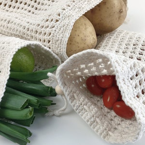 Puede incluir: Tres bolsas de malla de algod&oacute;n blanco para productos, que contienen diferentes frutas y verduras. Las bolsas son de algod&oacute;n natural y son reutilizables. La primera bolsa contiene patatas, la segunda bolsa contiene cebollas verdes y una lima, y la tercera bolsa contiene tomates rojos.