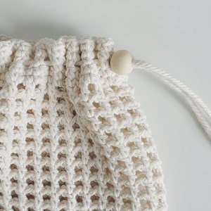 Puede incluir: Una bolsa de malla de crochet blanca con un cierre de madera. La bolsa est&aacute; hecha de un material suave y natural y tiene un dise&ntilde;o simple y elegante.