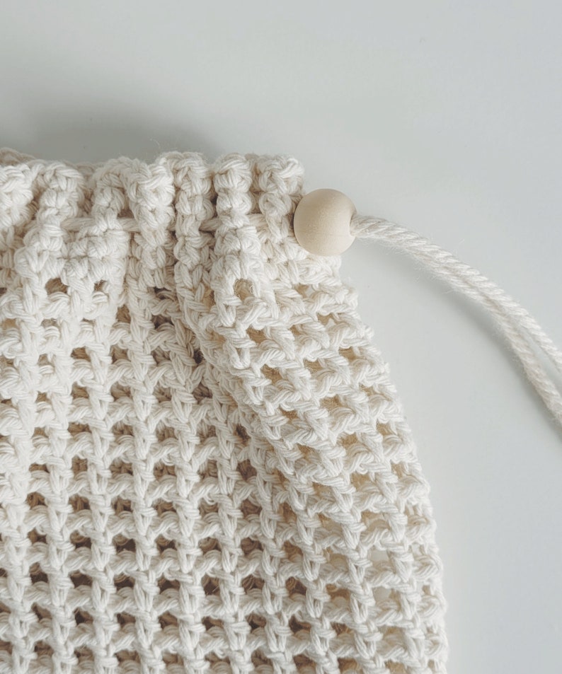 Puede incluir: Una bolsa de malla de crochet blanca con un cierre de madera. La bolsa est&aacute; hecha de un material suave y natural y tiene un dise&ntilde;o simple y elegante.