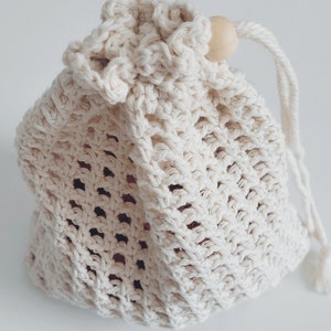 Puede incluir: Una bolsa de cord&oacute;n de crochet blanco con una cuenta de madera en la parte superior del cord&oacute;n.