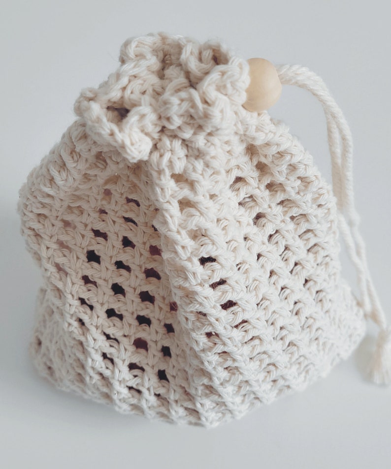 Puede incluir: Una bolsa de cord&oacute;n de crochet blanco con una cuenta de madera en la parte superior del cord&oacute;n.