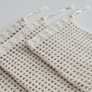 Puede incluir: Tres bolsas de malla de crochet beige con cuentas de madera en la parte superior de los cordones.