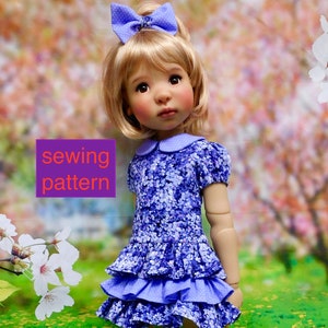 May include: A doll wearing a purple and white floral dress with a ruffled skirt and a purple bow in her hair. The doll is standing in a field of green grass with yellow flowers.