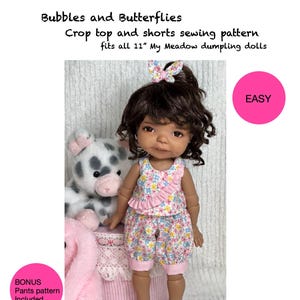 May include: A sewing pattern for a crop top and shorts for 11 inch dolls. The pattern is labeled "Bubbles and Butterflies" and is described as "easy". The pattern includes a bonus pants pattern. The doll is wearing a pink and floral print outfit.