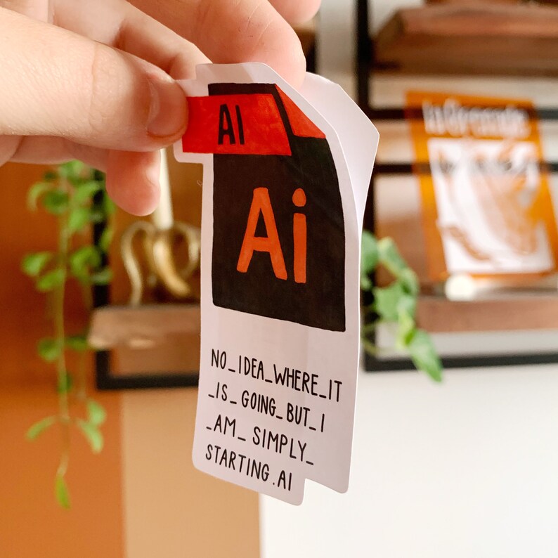 K&ouml;nnte beinhalten: Ein wei&szlig;er Aufkleber mit einem schwarzen und orangefarbenen Adobe Illustrator-Symbol und dem Text "NO_IDEA_WHERE_IT_IS_GOING_BUT_I_AM_SIMPLY_STARTING.AI"