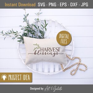 May include: A white pillow with the text "HARVEST blessings" in brown lettering and a small green sprig of leaves. The pillow is on a white wicker tray with a string of wooden beads.