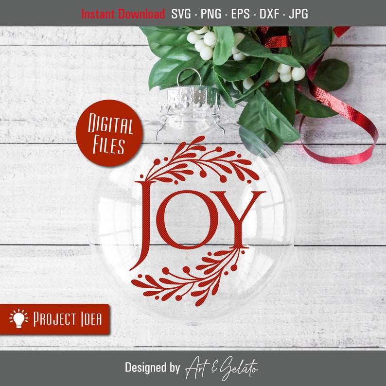 Op de afbeelding: Een transparante glazen kerstbal met een rood "JOY" ontwerp en rode bloemmotieven. De bal ligt op een houten oppervlak.