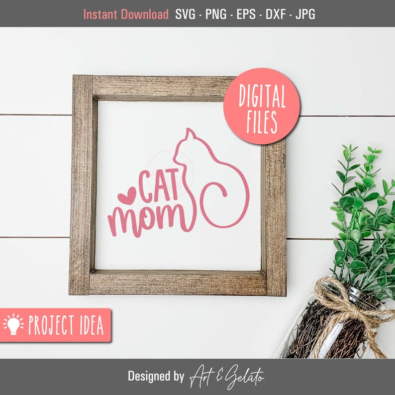 May include: A pink and white sign with the text "CAT MOM" and a pink silhouette of a cat. The sign is in a wooden frame and is sitting on a white surface.