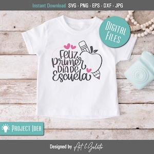 May include: White t-shirt with a pink apple, pencil, and hearts graphic. The text "Feliz primer dia de escuela" is written in gray on the shirt.